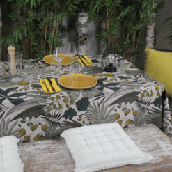 Photo d'ambiance nappe sur table Lombok, Emeraude : feuillage aux nuances de jaune, de turquoise et de beige sur un fond beige, feuillage avec des contours noirs