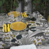 Photo d'ambiance nappe sur table Lombok, Emeraude : feuillage aux nuances de jaune, de turquoise et de beige sur un fond beige, feuillage avec des contours noirs 1